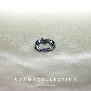 May include: A silver-colored ring with a floral design. The ring is set against a neutral background. The text "USAMA COLLECTION" and "Handcrafted Jewellery" are at the bottom of the image.