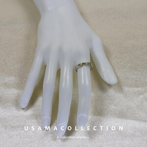 May include: A silver ring with a gold-colored floral design is displayed on a mannequin hand. The ring is worn on the ring finger. The brand name "USAMA COLLECTION" and the text "Handcrafted Jewellery" are visible at the bottom.