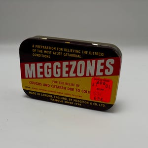 May include: A vintage tin of "Meggezones" cough drops, with a red and yellow label. The tin reads "For the relief of coughs and catarrh due to cold." The text also states "Made in London, England, by Meggeson & Co. Ltd. Famous since 1796."