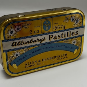 May include: A rectangular, vintage Allenburys Pastilles tin. The tin is gold with blue and white floral accents. Text on the tin reads "Allenburys Pastilles" and "Unique Glycerine & Blackcurrant Flavour". It contains 2 oz (56.7g).