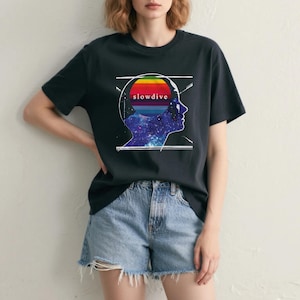 May include: Black t-shirt featuring a graphic of a head silhouette with a rainbow-colored brain and the word "slowdive." The brain graphic has a galaxy design. The model is wearing denim shorts.