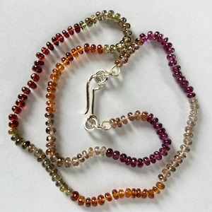 以下が含まれることがあります： 深紅から琥珀色、茶色や紫へと変化するグラデーションカラーのビーズネックレス。 小さな丸いビーズが連なり、銀色の留め金が付いています。