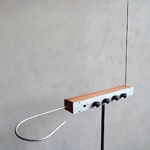 Puede incluir: Un instrumento musical theremin vintage. Cuenta con un cuerpo rectangular de madera y metal blanco con cuatro perillas negras y dos antenas. El instrumento está montado sobre un soporte negro sobre un fondo gris.