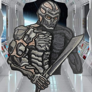 May include: A gray and black embroidered patch of a futuristic warrior with a sword. The warrior has a skeletal design and a menacing expression.