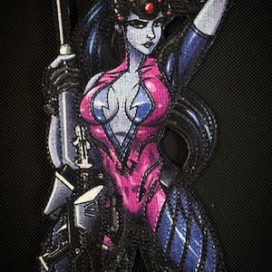 May include: Embroidered patch featuring a female character in a pink and blue bodysuit, holding a futuristic weapon. The character has blue hair and a black headpiece with a red gem. The patch is on a black textured background.