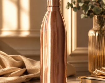 May include: A copper-colored, insulated water bottle with a rounded body and a matching cap. The bottle is made of shiny metal and reflects the light. The background includes a vase with greenery and a decorative wall.