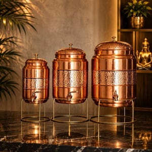 May include: Three cylindrical copper beverage dispensers of varying sizes, each featuring a hammered texture band, a matching lid with a small knob, a metal spigot at the base, and a thin gold-toned wire stand for elevated placement.