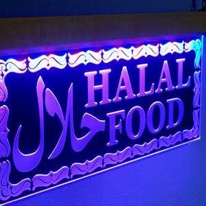 May include: A black and silver LED sign with the words "HALAL FOOD" in white lettering. The sign has a decorative border and a purple and blue glow.