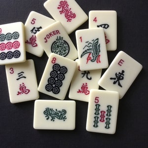 May include: A collection of white mahjong tiles with black and red Chinese characters and symbols. The tiles include numbers 1 through 8, the character for 'Joker', and the character for 'East'.