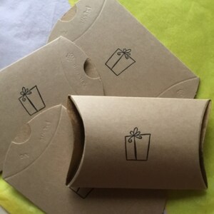 May include: Four brown cardboard gift boxes with a small gift box design printed on each. The boxes are stacked on top of each other and are sitting on a yellow piece of tissue paper.