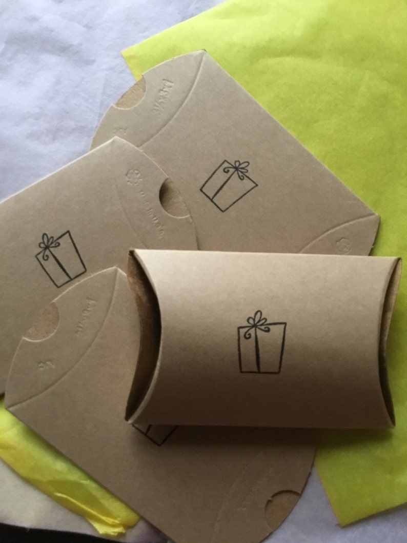 May include: Four brown cardboard gift boxes with a small gift box design printed on each. The boxes are stacked on top of each other and are sitting on a yellow piece of tissue paper.