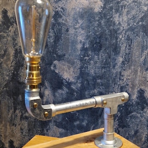 A modern industrial steampunk decor style desk lamp made from galvanized steel pipe and a wooden base.