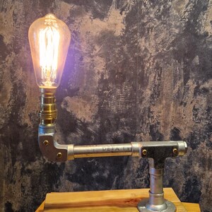 Industrial-style table lamp featuring a vintage-style filament bulb (not included) a galvanized steel pipe arm, and a rustic wooden base. Perfect for adding a touch of modern farmhouse or steampunk aesthetic to your home.