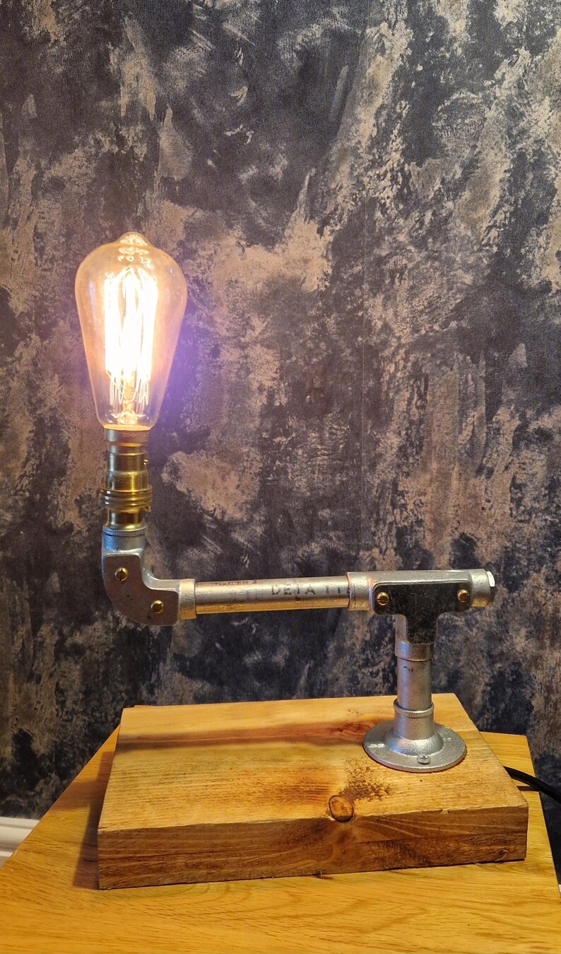Industrial-style table lamp featuring a vintage-style filament bulb (not included) a galvanized steel pipe arm, and a rustic wooden base. Perfect for adding a touch of modern farmhouse or steampunk aesthetic to your home.
