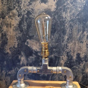 A modern industrial steampunk decor style desk lamp made from galvanized steel pipe and a wooden base.