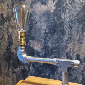 A modern industrial steampunk decor style desk lamp made from galvanized steel pipe and a wooden base.