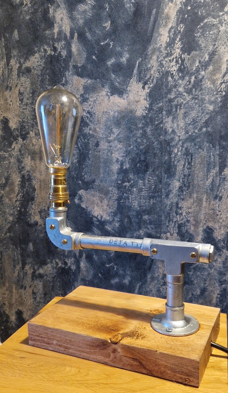 A modern industrial steampunk decor style desk lamp made from galvanized steel pipe and a wooden base.