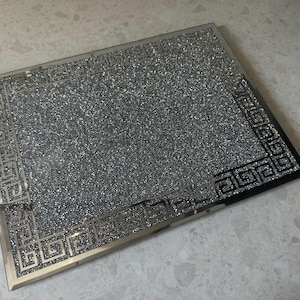 Könnte beinhalten: Ein silbernes Tablett mit einem schwarzen und weißen geometrischen Muster an der Kante. Das Tablett ist mit Glitzer bedeckt.