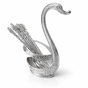 May include: A silver swan-shaped serving piece holding several small spoons. The swan has detailed feather and eye designs. The spoons have decorative handles. The serving piece is made of a shiny metal and sits on a white surface.