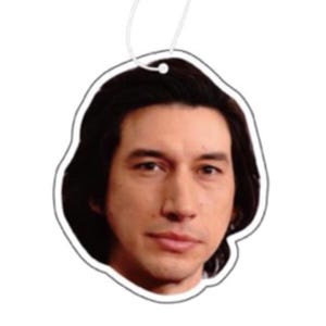 May include: A car air freshener featuring a close-up photo of a man with dark hair and a serious expression.