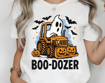 Peut inclure: T-shirt blanc avec un motif sur le thème d'Halloween. Le dessin représente un fantôme de dessin animé conduisant un bulldozer orange avec des citrouilles. Le texte "BOO-DOZER" est imprimé en noir en dessous, avec des chauves-souris et des étoiles.