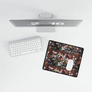 May include: A computer setup featuring a white keyboard, mouse, and a floral-patterned mousepad. The mousepad has a dark brown border and is filled with colorful flowers. A computer monitor displays the time.