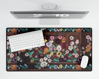 May include: A rectangular desk mat with a floral design featuring a variety of colorful flowers on a dark brown background. A white keyboard and mouse are on the mat, with a computer monitor above.