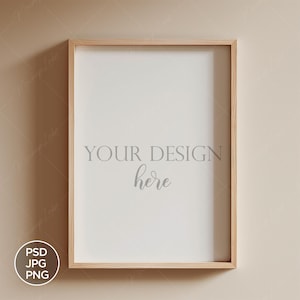Puede incluir: Un marco de madera clara con un paspartú blanco y el texto "YOUR DESIGN here" en el centro. El marco está colgado en una pared beige claro.