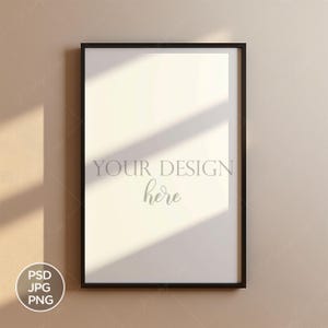 Peut inclure: Un cadre photo noir avec un passe-partout blanc et un fond blanc. Le cadre est accroché à un mur beige. Le texte "YOUR DESIGN here" est visible au centre du cadre.