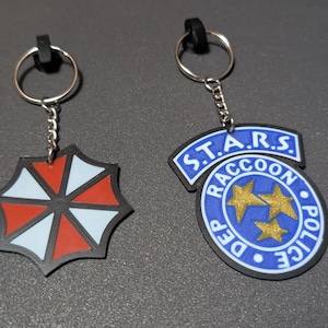 Resident Evil Schlüsselanhänger Set | Umbrella Corporation Logo & S.T.A.R.S. Waschbär Polizeimarke | 3D gedrucktes Gamer Geschenk Horror Cosplay Accessoire