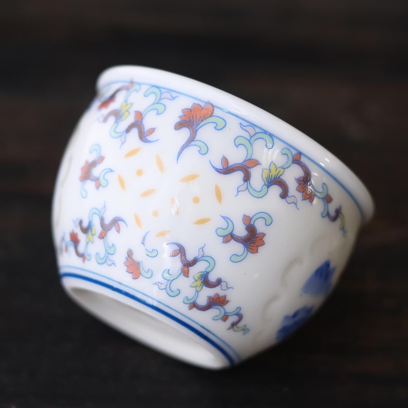 Może przedstawiać: Biała ceramiczna miska z niebieską obw&oacute;dką i skomplikowanymi wzorami kwiatowymi w kolorze pomarańczowym, niebieskim i ż&oacute;łtym. Miska ma zaokrąglony kształt i delikatny design, idealna do serwowania małych porcji.