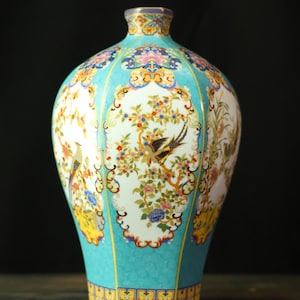 Puede incluir: Un jarrón de cerámica decorativo con fondo turquesa y diseños florales y de aves. El jarrón tiene un cuello estrecho y un cuerpo ancho, con detalles dorados. La obra de arte detallada incluye flores y aves coloridas, creando una estética elegante.