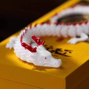 May include: A white and red dragon figurine with intricate details, resting on a yellow surface. The dragon has red horns and accents along its spine. The figurine is a decorative item.