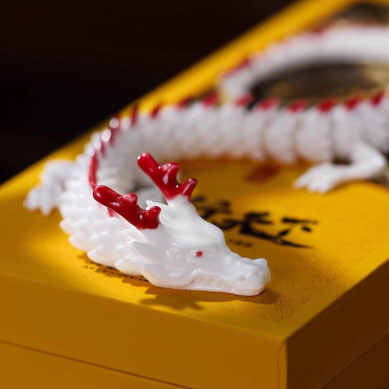 May include: A white and red dragon figurine with intricate details, resting on a yellow surface. The dragon has red horns and accents along its spine. The figurine is a decorative item.