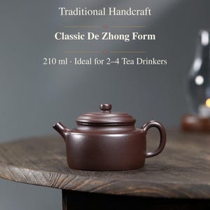May include: A dark brown clay teapot with a lid, featuring a spout and a curved handle. The text above the teapot reads: Traditional Handcraft, Classic De Zhong Form, 210 ml · Ideal for 2–4 Tea Drinkers. The teapot has a smooth, matte finish.