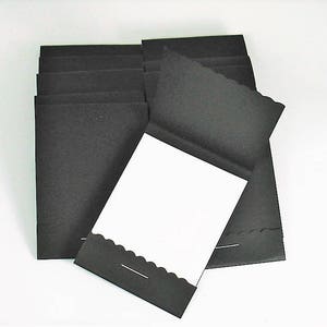 May include: A stack of black cardstock paper with scalloped edges. The top sheet is folded in half to reveal a blank white interior.