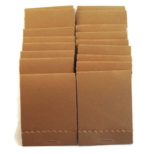 May include: A stack of brown matchbooks with a scalloped edge and a staple. The matchbooks are arranged in two columns, with the match heads facing up. The paper has a natural, unbleached appearance.