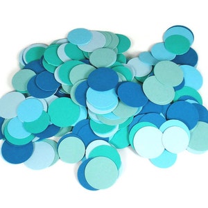 May include: A pile of blue and green paper circles, scattered on a white background. The circles are various sizes and shades of blue and green.