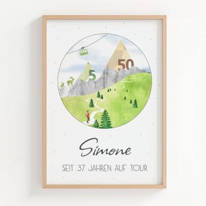 Pode incluir: Uma impressão emoldurada com uma ilustração em aquarela de uma cena de montanha com um caminho sinuoso, árvores e um teleférico. Os números 5 e 50 estão nas montanhas. O nome "Simone" e o texto "SEIT 37 JAHREN AUF TOUR" estão abaixo.