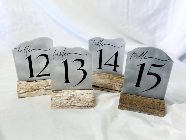 May include: Four gray table number signs with black text on wooden bases. The signs read "table 12", "table 13", "table 14", and "table 15".