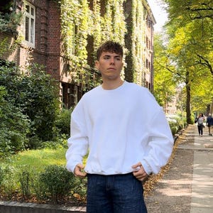 May include: A white crew neck sweatshirt with long sleeves and a relaxed fit. The sweatshirt is made of a soft, comfortable fabric.