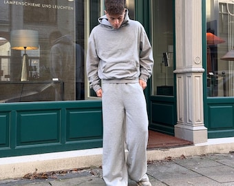 May include: A light gray matching set consisting of a long-sleeved hooded sweatshirt with a front kangaroo pocket and wide-leg sweatpants. The hoodie features a drawstring-free hood and ribbed cuffs, while the pants have a relaxed, loose fit.
