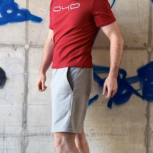 May include: A red short-sleeved t-shirt with the white text O40 printed on the chest, paired with light grey shorts featuring side pockets. The t-shirt has a crew neckline and the shorts reach above the knee, providing a casual athletic look.
