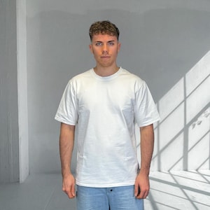 May include: A plain white short-sleeved t-shirt with a crew neckline, worn with light blue denim jeans. The t-shirt has a standard fit and a straight hem, whilst the jeans feature a visible button fastening at the waist.