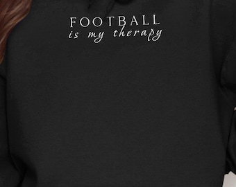Może przedstawiać: Czarna bluza z kapturem z napisem "FOOTBALL is my therapy" w białym kolorze.