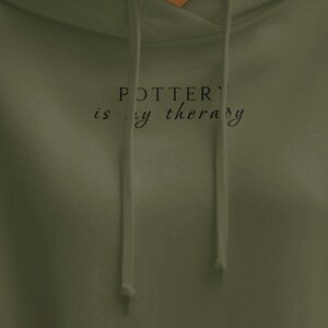 Puede incluir: Una sudadera con capucha verde con el texto "POTTER'S is my therapy" impreso en la parte delantera.