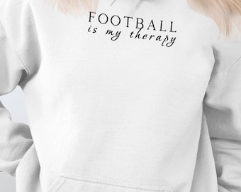 Może przedstawiać: Biała bluza z kapturem z napisem "FOOTBALL is my therapy" czarnymi literami.