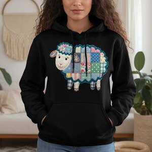 May include: Black hoodie featuring a colorful patchwork sheep design. The sheep has a blue and white scalloped outline, with a floral and gingham pattern. The hoodie has a kangaroo pocket and a drawstring hood.
