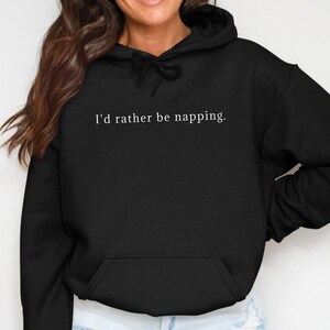 Pode incluir: Camisola de moletom com capuz preta com o texto "I'd rather be napping." impresso em branco na frente.