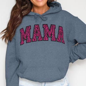 May include: A blue hooded sweatshirt with the word "MAMA" in large, pink zebra print letters across the chest. The sweatshirt has a front pocket and a drawstring hood.